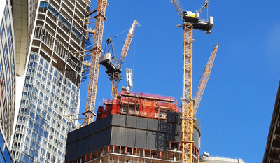 Mehrere gelbe Baukräne arbeiten an der Baustelle eines Hochhauses vor einem klaren blauen Himmel.