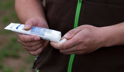 Eine Person hält eine geöffnete Tube Creme und drückt etwas davon auf die Finger.