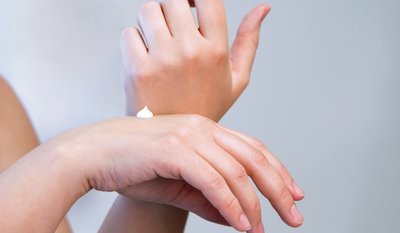 Eine Hand trägt eine kleine Menge weißer Creme auf den Handrücken der anderen Hand auf.