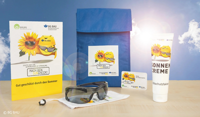 Eine Sammlung von Sonnenschutzartikeln, darunter eine Sonnencremetube, eine Packung, eine Brille, ein Brillenetui und eine Informationsbroschüre mit Sonnenblumen- und Helmillustrationen, vor einem blauen Himmel mit Wolken.