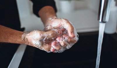 Hände werden unter fließendem Wasser mit Seife eingeseift.