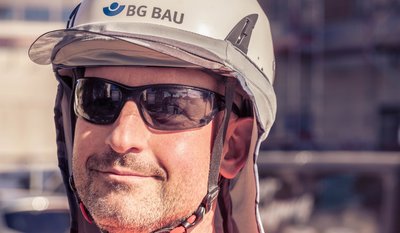 Eine Person trägt einen weißen Bauhelm mit der Aufschrift "BG BAU" und eine Sonnenbrille.